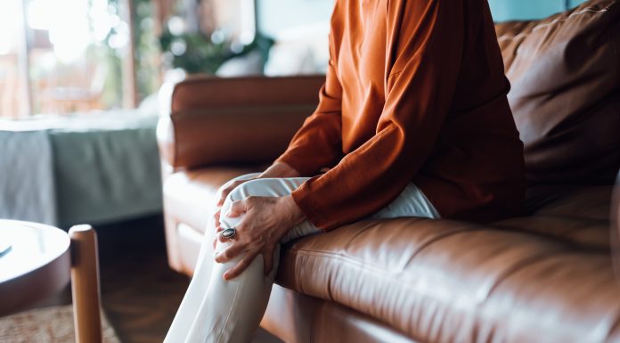 Cropped shot of a distraught senior Asian woman feeling unwell, suffering from pain in leg while sitting on sofa in the living room at home. Elderly and health issues concept