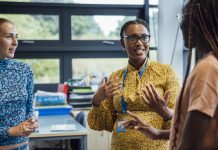 A shot of a mid-adult secondary school teacher talking with her sixth form students in class, they are wearing casual clothing and discussing what they learned in class, in a school in Gateshead, England.