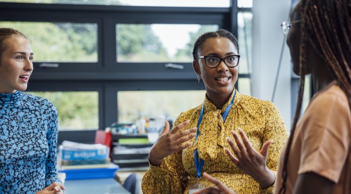 A shot of a mid-adult secondary school teacher talking with her sixth form students in class, they are wearing casual clothing and discussing what they learned in class, in a school in Gateshead, England.