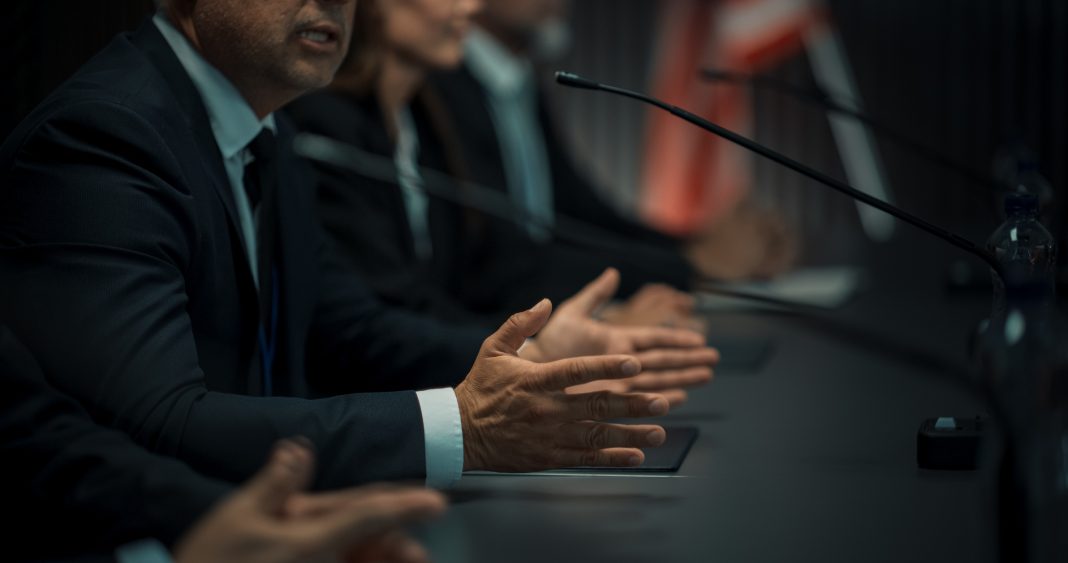 Close Up On Hands of Caucasian Male Organization Representative Speaking at Economic Conference. Head Of USA Delegation Delivering Speech at International Political Summit. Diverse Delegates Listening