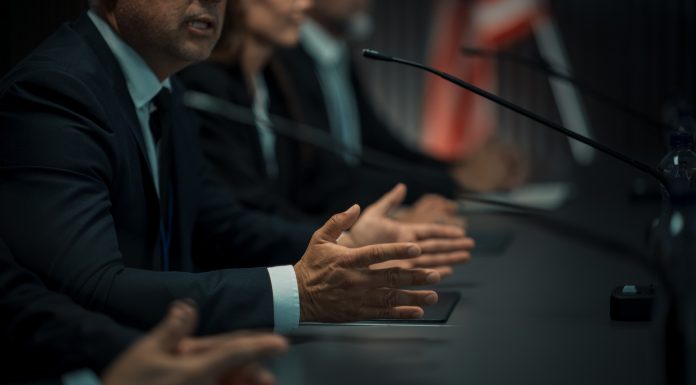 Close Up On Hands of Caucasian Male Organization Representative Speaking at Economic Conference. Head Of USA Delegation Delivering Speech at International Political Summit. Diverse Delegates Listening