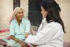 Female doctor examining indian senior adult woman with stethoscope during house visit in.