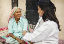 Female doctor examining indian senior adult woman with stethoscope during house visit in.