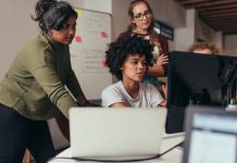 Software engineers working on project and programming in company. Startup business group working as team to find solution to problem. Woman programmer working on computer with colleagues standing by.