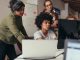 Software engineers working on project and programming in company. Startup business group working as team to find solution to problem. Woman programmer working on computer with colleagues standing by.