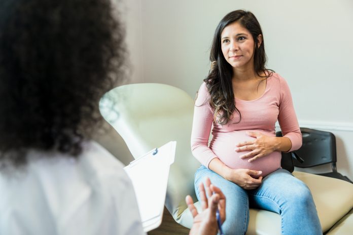 Expectant mother touches abdomen while listening to unrecognizable doctor