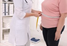 Nutritionist measuring overweight woman's waist with tape in clinic, closeup