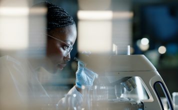 Scientist, microscope and analysis in lab for healthcare, innovation and development in stem cell research. Black woman, investigation and experiment with biotech for dna, exam or test for bacteria