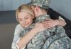 smiling mother hugging grown son in military uniform at home