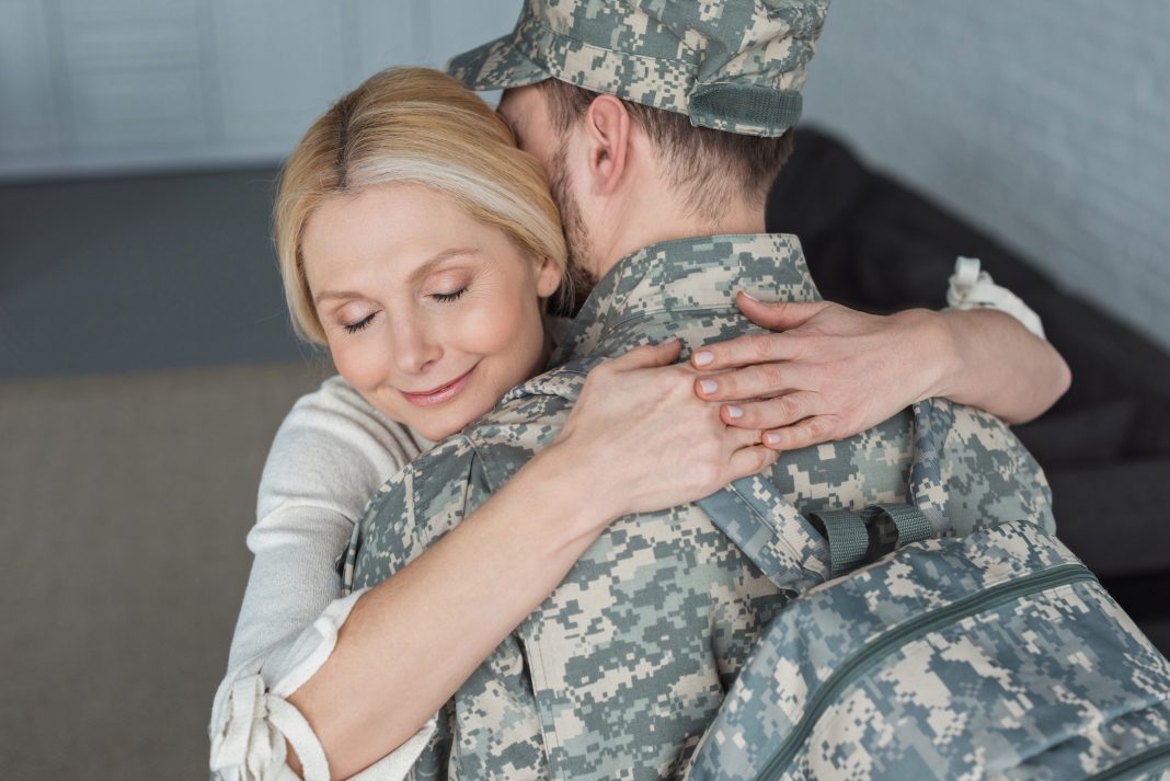 smiling mother hugging grown son in military uniform at home