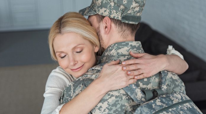 smiling mother hugging grown son in military uniform at home