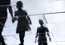 Blurry reflection shadow silhouette in a puddle of siblings and a parent walking wet city street