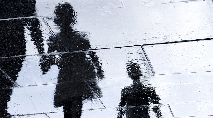 Blurry reflection shadow silhouette in a puddle of siblings and a parent walking wet city street