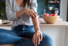 Young woman scratching her arm while sitting on the stool in the home kitchen.