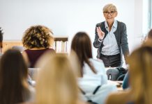 Happy senior teacher talking to large group of college students in amphitheater.