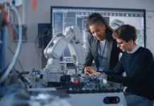 Male Student Engineer Discussing Ideas with Black Teacher while Working with Computer Processor. Man Uses Screwdriver. High-Tech Science and Engineering Concept. Medium Shot