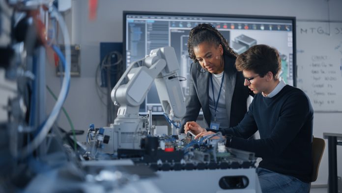 Male Student Engineer Discussing Ideas with Black Teacher while Working with Computer Processor. Man Uses Screwdriver. High-Tech Science and Engineering Concept. Medium Shot