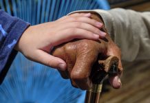 Grandchild holding grandparent's hand. Grandfather leaning on a walking stick. Dark skin toned grandfather with light skin toned grandchild. Mixed race family.