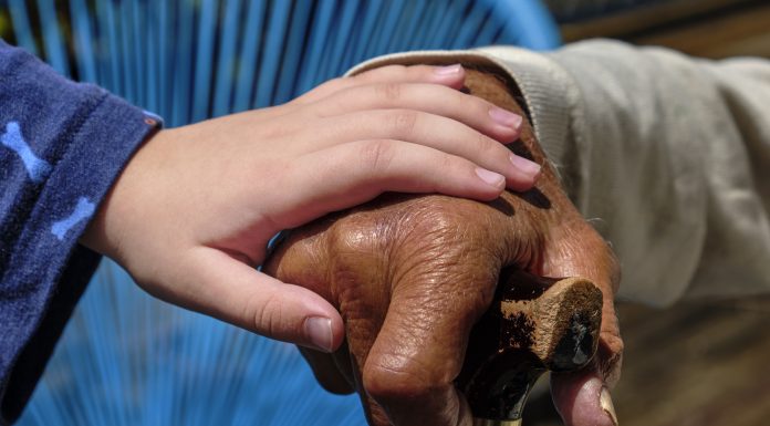 Grandchild holding grandparent's hand. Grandfather leaning on a walking stick. Dark skin toned grandfather with light skin toned grandchild. Mixed race family.