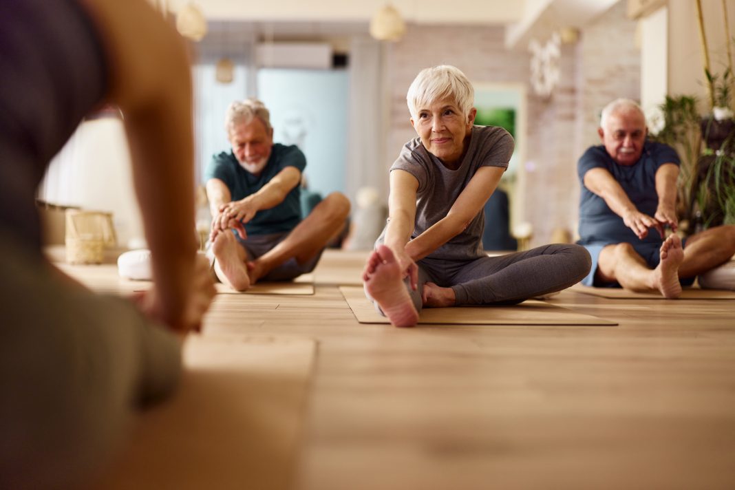 Group of mature people doing stretching exercises with their coach during a Yoga class in a studio. Focus is on senior woman. Copy space.